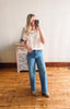 Woman taking a mirror selfie wearing a white t-shirt and blue jeans in a room with wooden flooring.