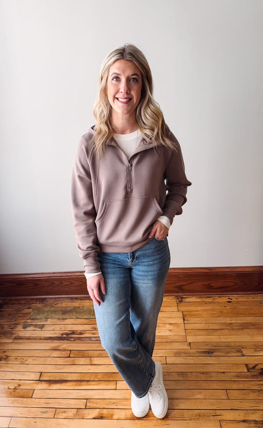 Woman wearing a pink zip-up hoodie and blue jeans standing on a wooden floor.