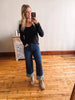 Woman taking a mirror selfie wearing a black top and blue jeans in a room with wooden flooring.