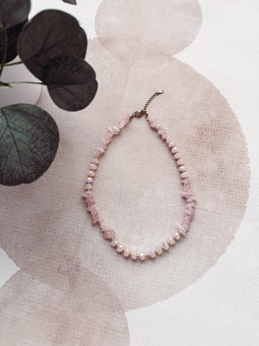 Pink beaded necklace on a textured surface with eucalyptus leaves in the background