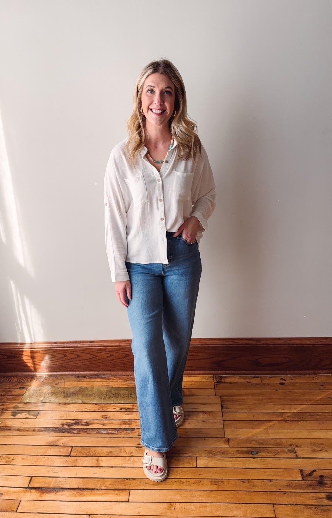 Woman wearing a white blouse and blue jeans standing on a wooden floor with a white wall background