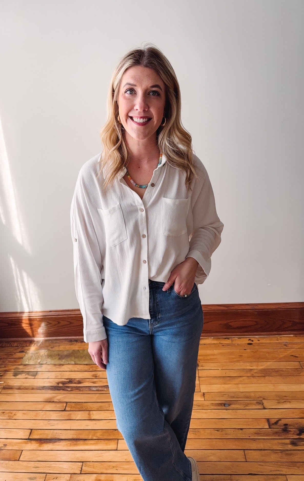 Woman wearing a white shirt and blue jeans standing on a wooden floor with a white wall background