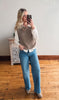 Woman taking a mirror selfie wearing a brown sweater vest, white shirt, blue jeans, and beige shoes.