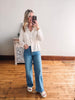 Woman taking a mirror selfie wearing a white button-up shirt and blue jeans in a room with wooden flooring.