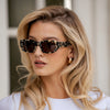 Woman wearing leopard print sunglasses and a white top outdoors.