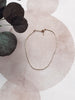 Delicate necklace on a textured surface with leaves in the background