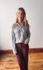 Woman wearing a gray button-up shirt and maroon pants standing in a room with wooden flooring.
