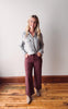 Woman wearing a light gray shirt and maroon pants standing on a wooden floor.