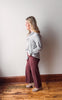 Person wearing a gray shirt and maroon pants standing against a white wall.