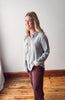 Woman wearing a gray shirt and maroon pants standing against a white wall.