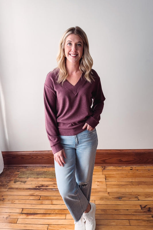 Woman wearing a maroon sweater and light blue jeans standing on a wooden floor.