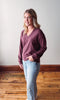 Woman wearing a maroon sweater and light blue jeans standing on a wooden floor.