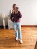 Woman taking a mirror selfie wearing a maroon sweater and light blue jeans in a room with wooden flooring.