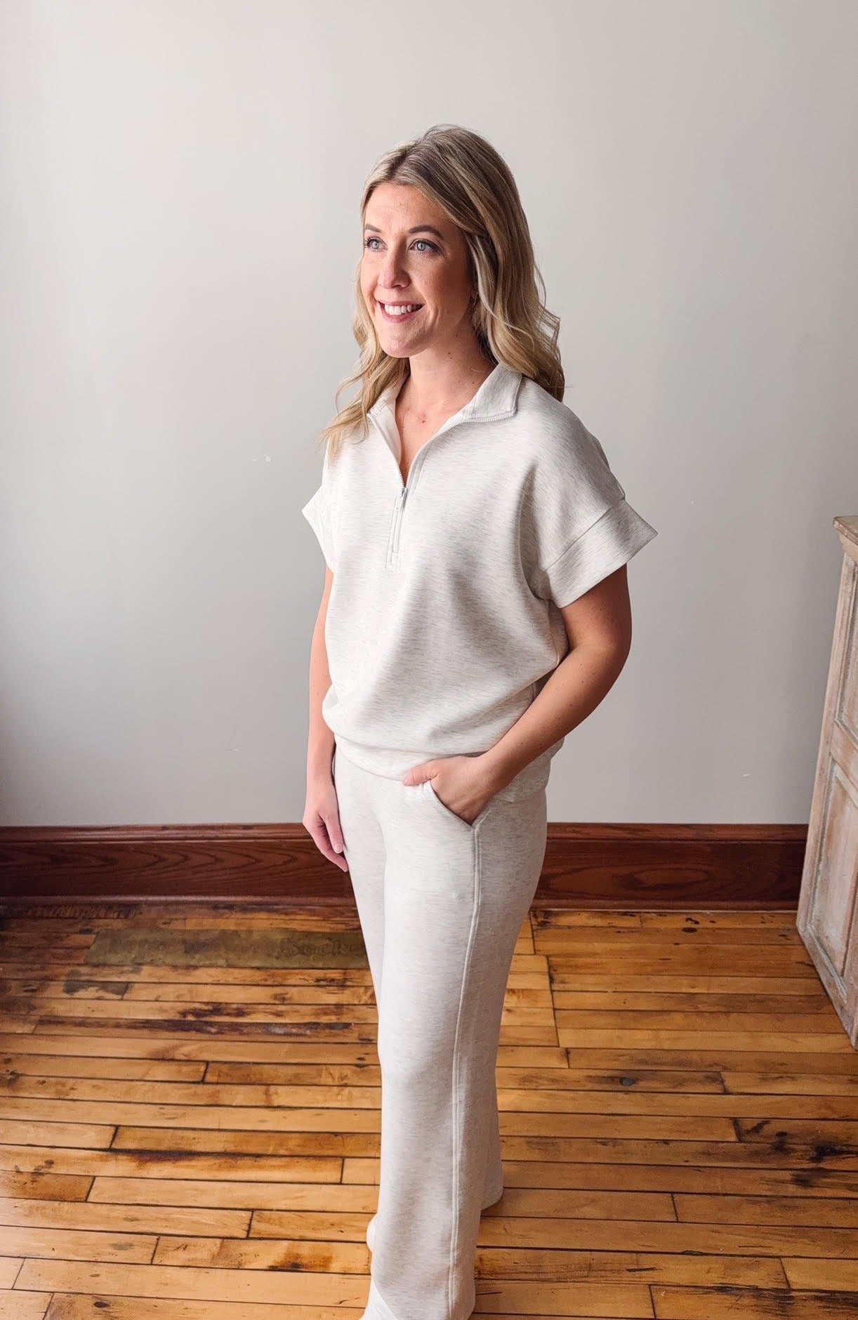 Woman in a white outfit standing on a wooden floor with a plain wall background