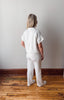 Person wearing a white outfit standing on a wooden floor against a plain wall.