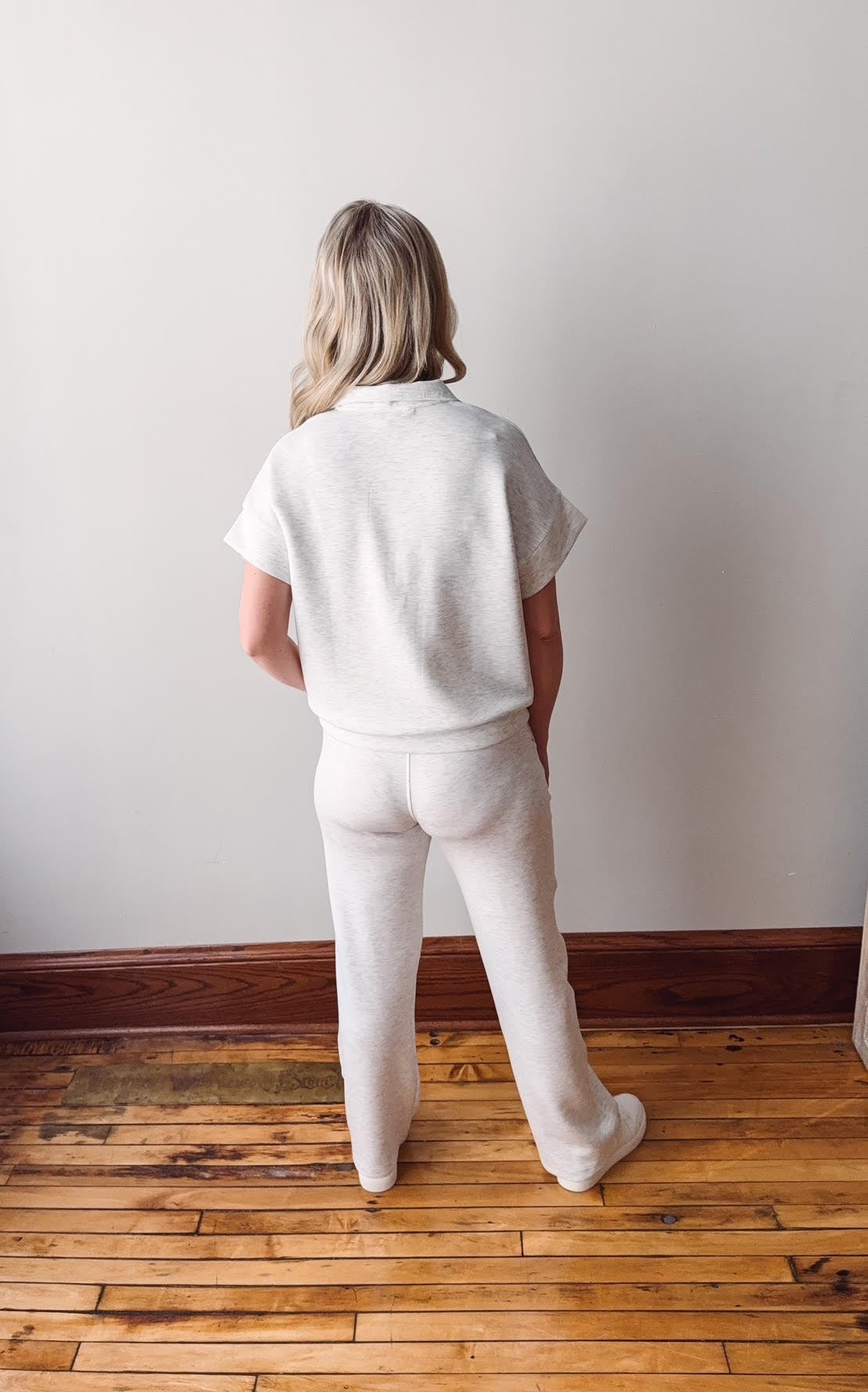 Person wearing a white outfit standing on a wooden floor against a plain wall.