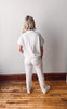 Person wearing a white outfit standing on a wooden floor against a plain wall.