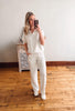 Woman taking a mirror selfie wearing a white outfit in a room with wooden flooring.