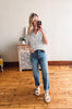 Woman taking a mirror selfie wearing a white lace top and blue jeans in a room with wooden flooring.