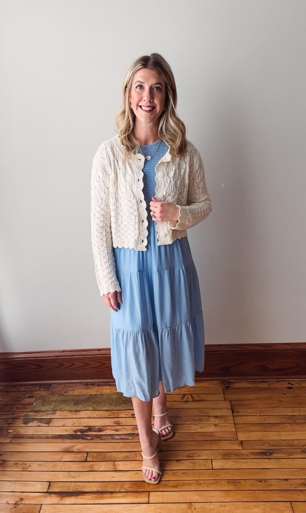 Woman wearing a light blue dress with a white cardigan in a room with wooden flooring.