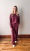 Woman wearing a burgundy outfit standing on a wooden floor against a white wall