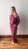 Woman wearing a maroon tracksuit with white stripes on a wooden floor.