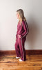 Woman wearing a burgundy tracksuit with white piping against a plain wall.