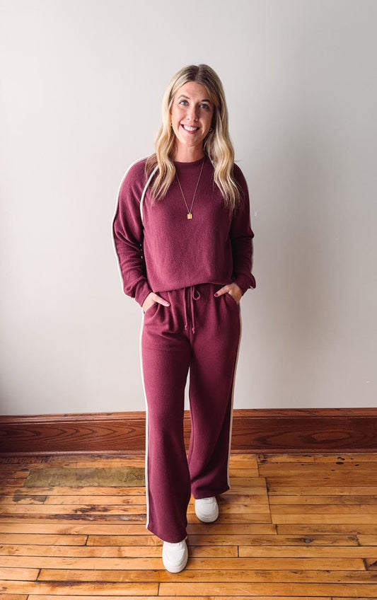 Woman wearing a maroon tracksuit standing on a wooden floor with a white wall background