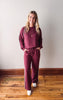 Woman wearing a maroon tracksuit standing on a wooden floor with a white wall background