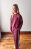 Woman wearing a maroon tracksuit with white stripes on a wooden floor.