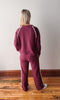 Person wearing a burgundy tracksuit with white stripes on a wooden floor and light gray wall.