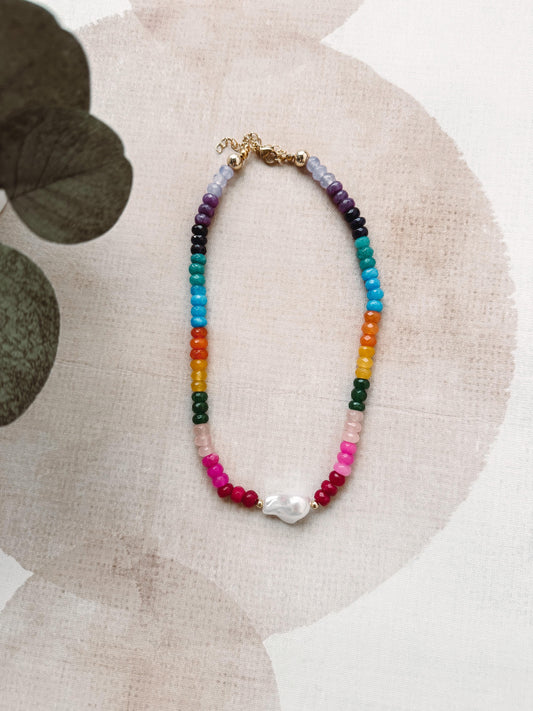 Colorful beaded necklace with a pearl pendant on a floral-patterned surface