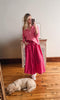 Woman in pink shirt and skirt standing next to a dog on a wooden floor.