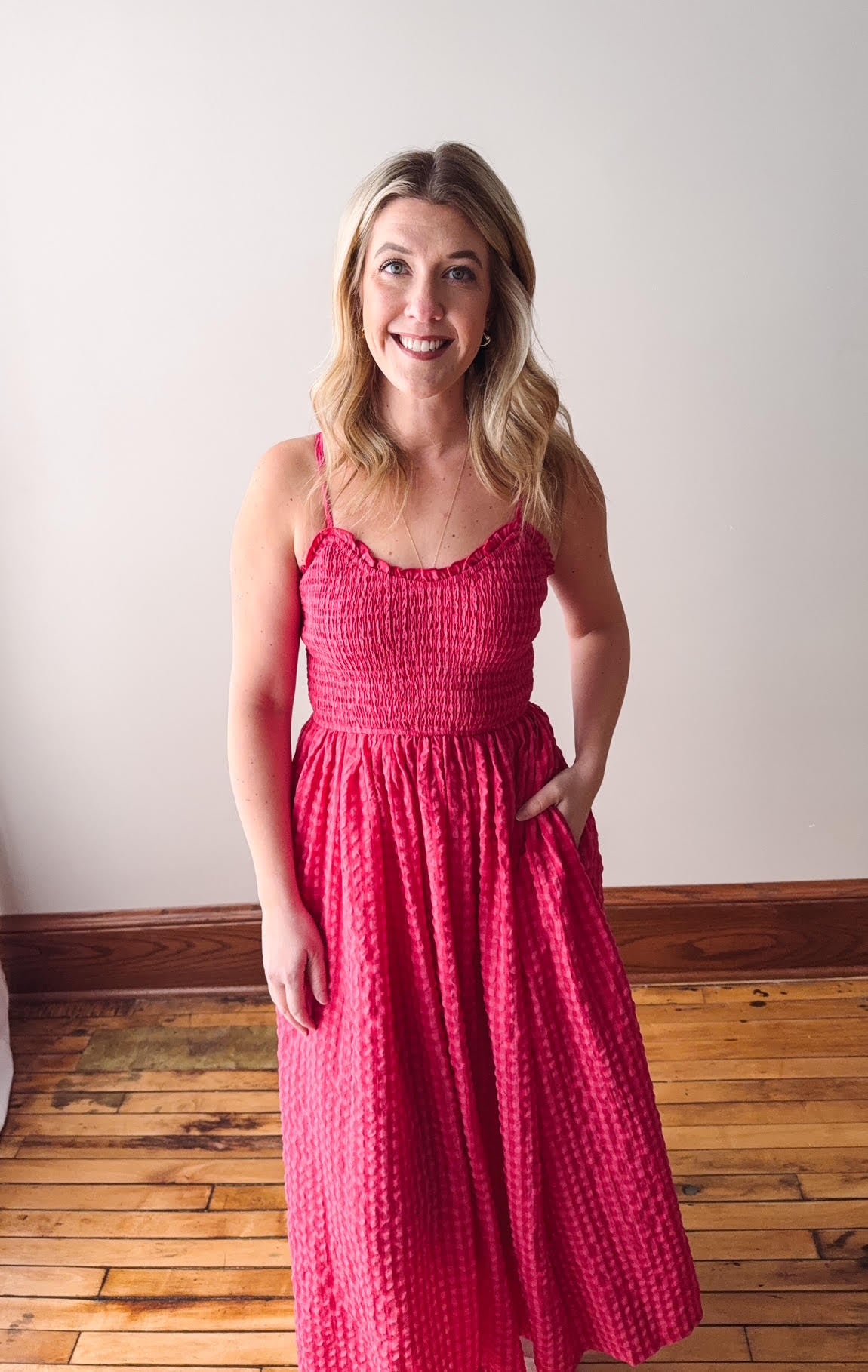 Woman wearing a pink dress standing on a wooden floor with a white wall background