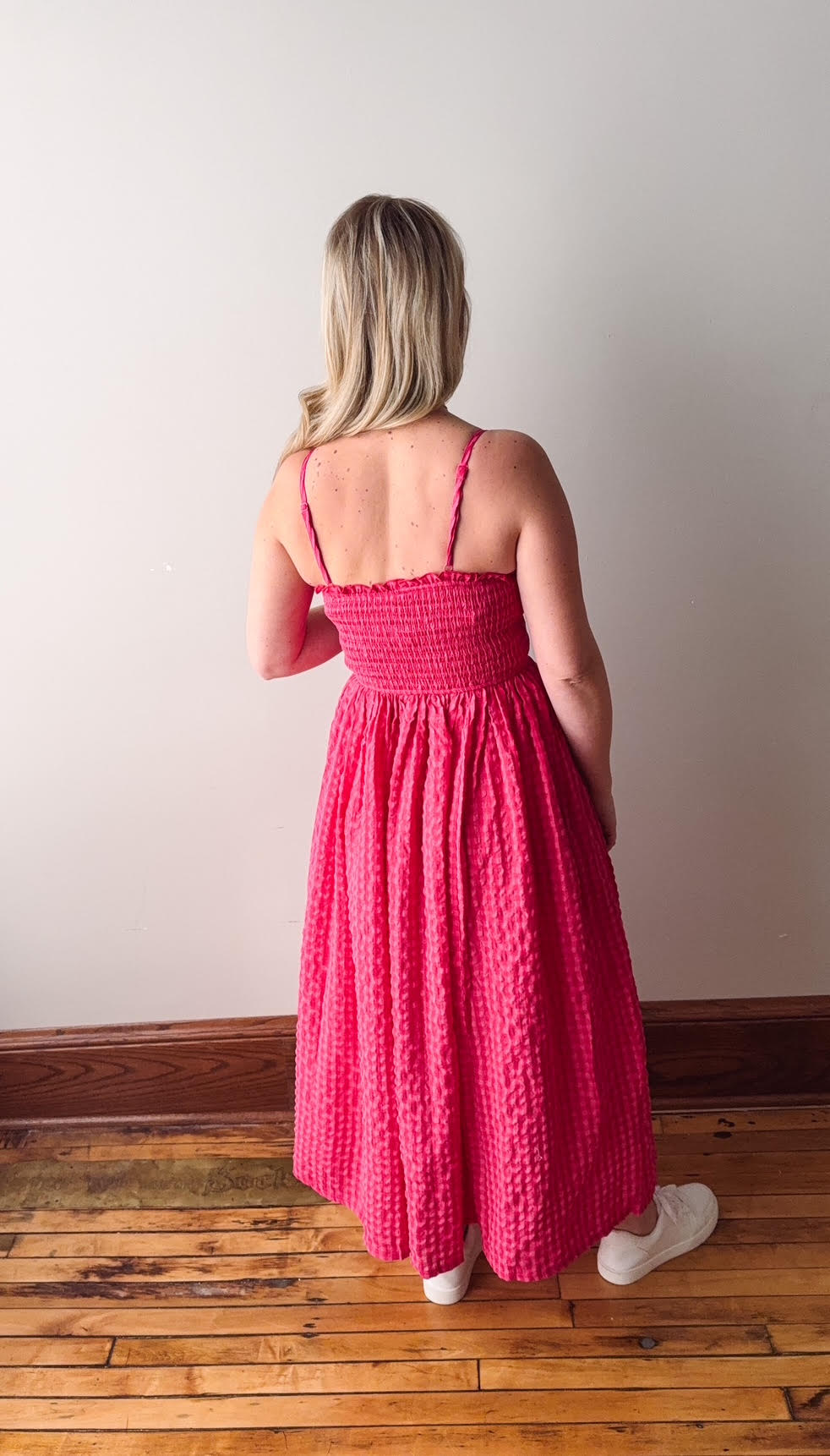 Woman wearing a pink dress standing on a wooden floor with a white wall background