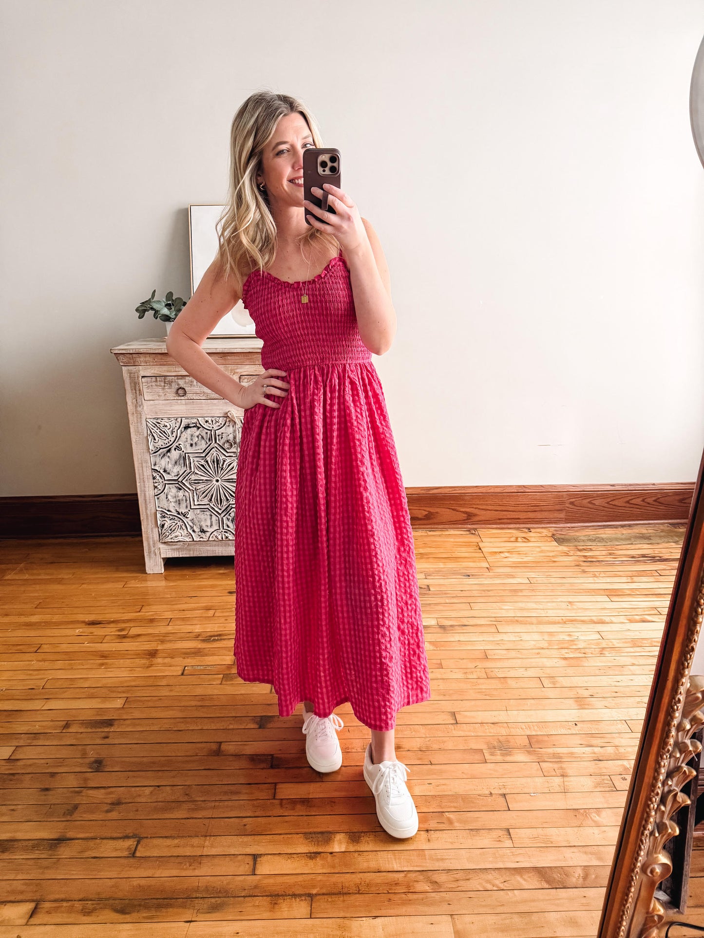 Woman in a pink dress taking a mirror selfie in a room with wooden flooring.