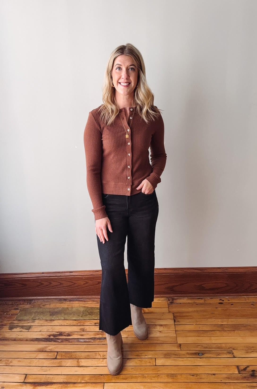 Woman wearing a brown button-up shirt and black pants standing on a wooden floor.