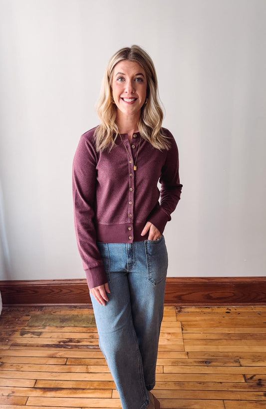 Woman wearing a maroon button-up shirt and blue jeans standing on a wooden floor.