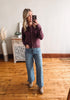 Woman taking a mirror selfie wearing a purple shirt and blue jeans in a room with wooden flooring and a decorative cabinet.