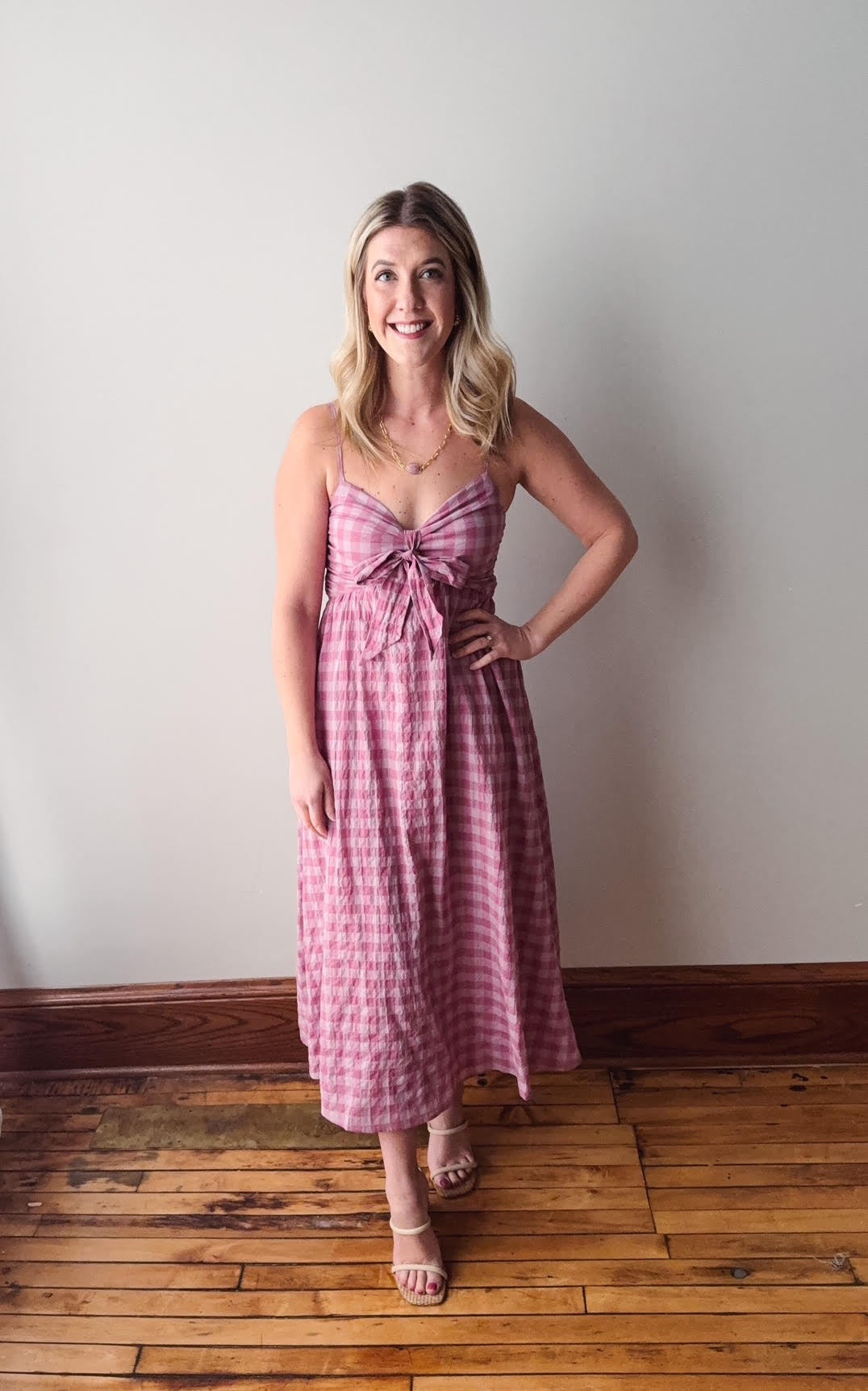 Woman wearing a pink checkered dress standing against a plain wall.