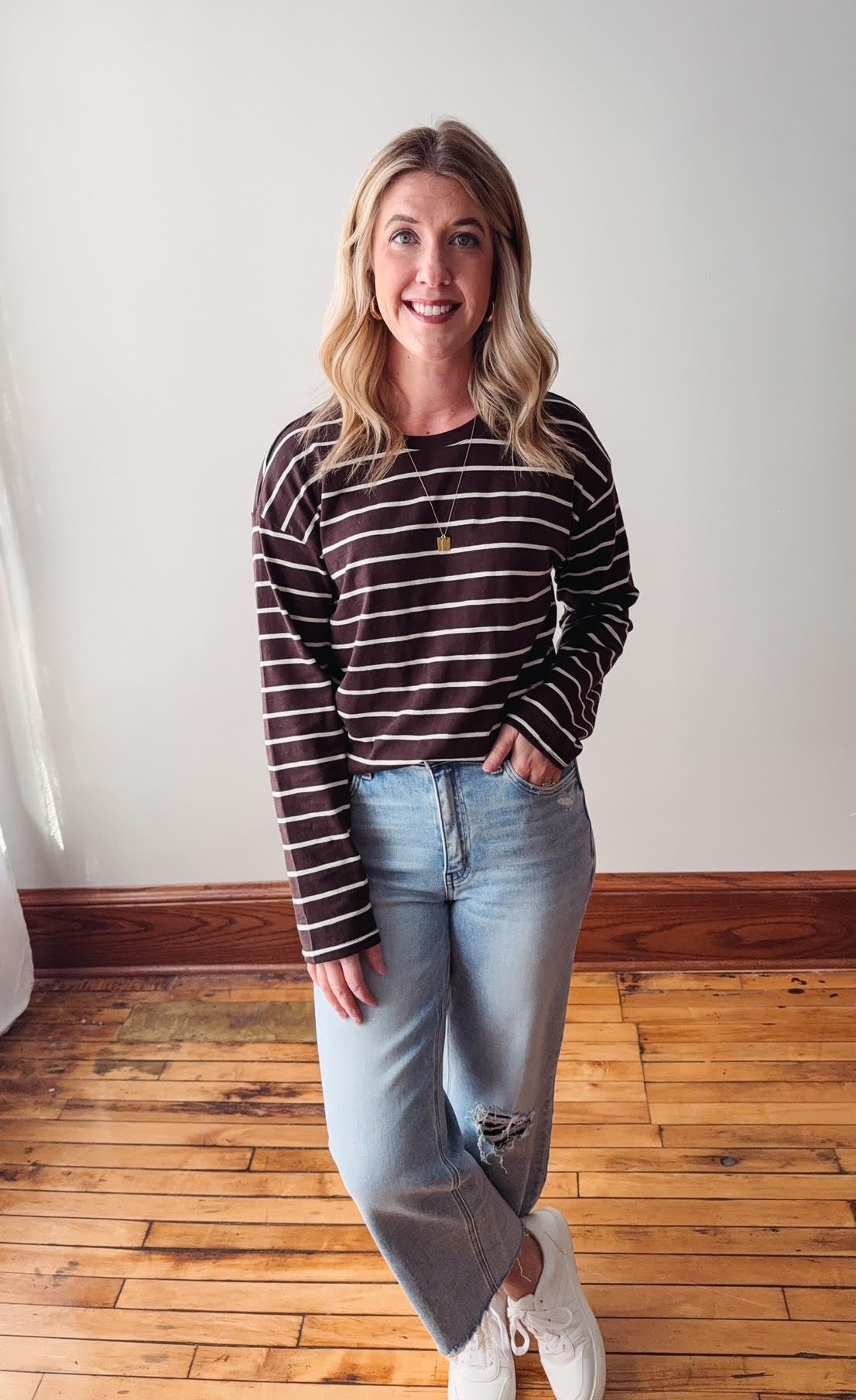 Woman wearing a striped long-sleeve shirt and jeans standing on a wooden floor.