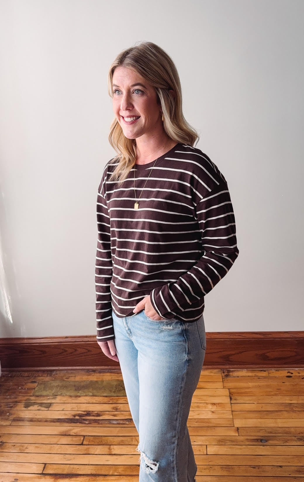 Woman wearing a striped sweater and light blue jeans standing on a wooden floor.