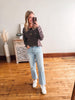Woman taking a mirror selfie wearing a striped sweater and jeans in a room with wooden flooring.