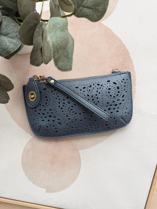Blue perforated handbag on a light background with green leaves