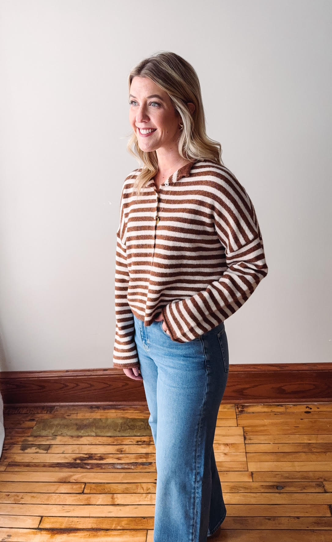 Woman wearing a striped sweater and jeans standing in a room with wooden flooring.