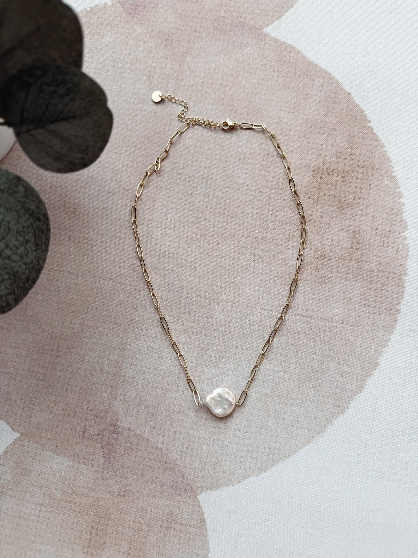 Gold chain necklace with a pearl pendant on a textured surface