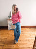 Woman taking a mirror selfie wearing a pink sweater and blue jeans in a room with wooden flooring.