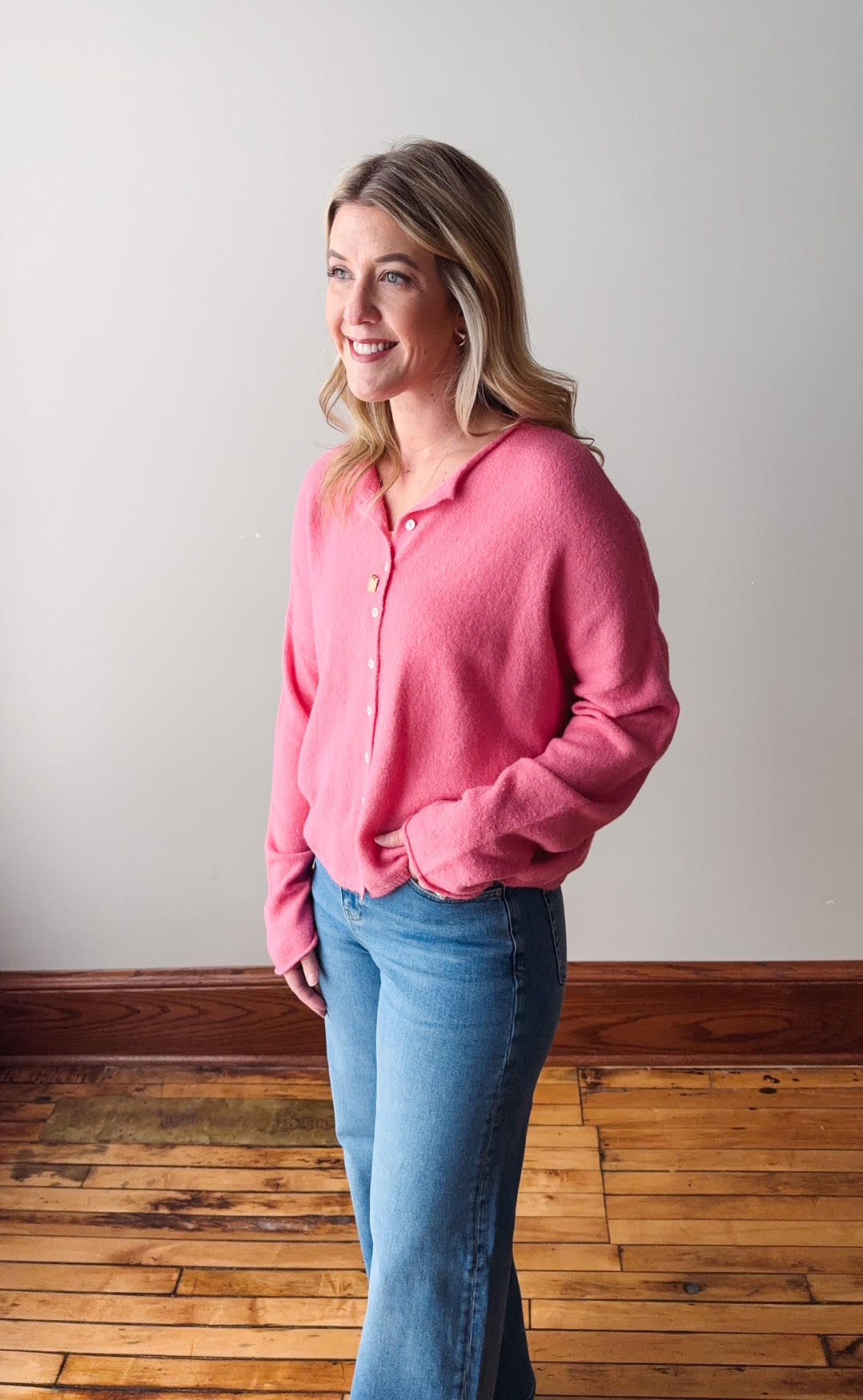 Woman wearing a pink sweater and blue jeans standing against a plain wall.