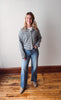 Woman wearing a striped shirt and jeans standing on a wooden floor with a white wall background