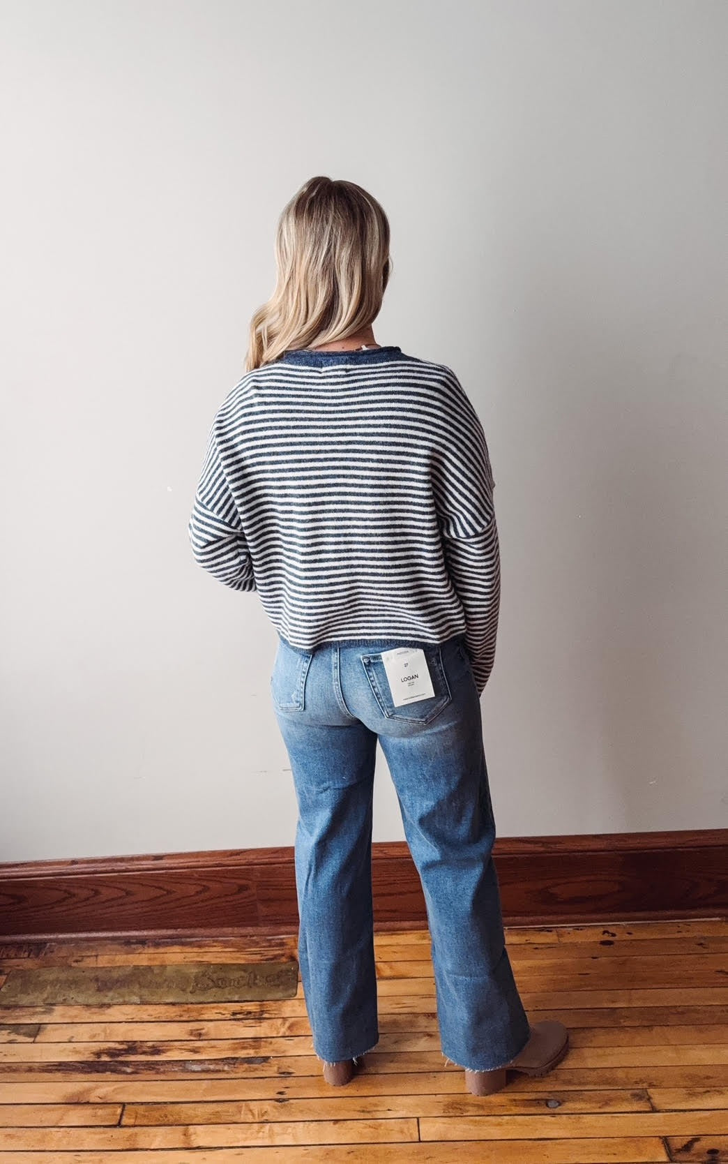 Person wearing a striped sweater and blue jeans standing against a plain wall.
